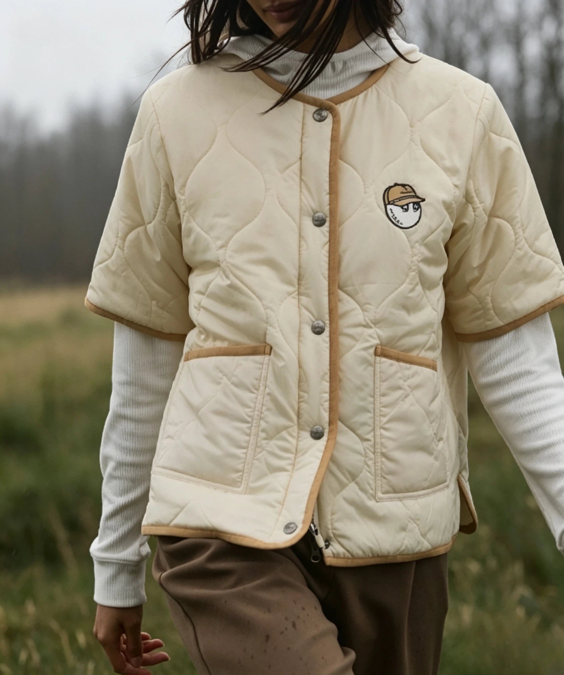 Malbon women's short-sleeve insulated padded golf jacket in Cream, lifestyle view