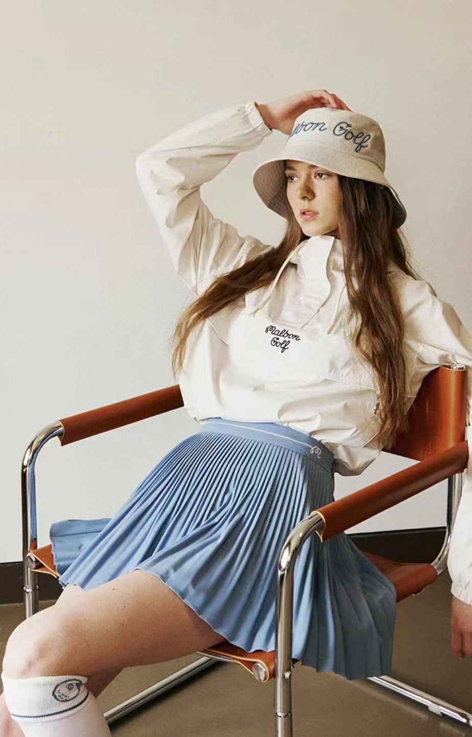Seated model wearing blue Malbon solid pleated golf skort